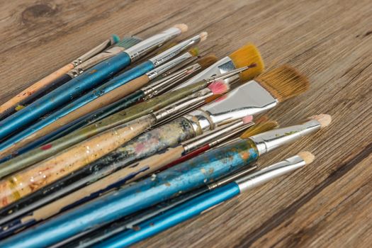 Artist paint brushes over rustic wooden texture. Top view with copy space.