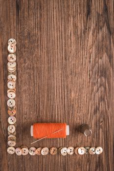 Sewing needle threaded with a orange thread ready for sewing. Buttons frame. Scene on a rustic wooden table. Top view with copy space.