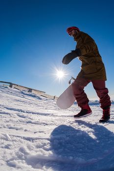 Snowboarder walking through deep fresh snow against blue sky.