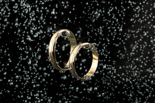 Two engagement golden rings in the water with air bubbles