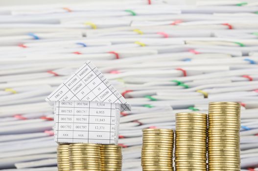 House on pile of gold coins with step pile of gold coins have blur overload of confused paperwork with colorful paperclip as background.