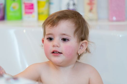 Happy cute little girl taking spa bath at home in water with foam and bubbles