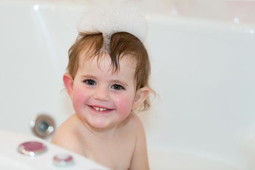 Happy cute little girl taking spa bath at home in water with foam and bubbles
