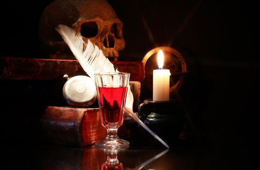 Medieval still life. Old books and quill near wine and lighting candle