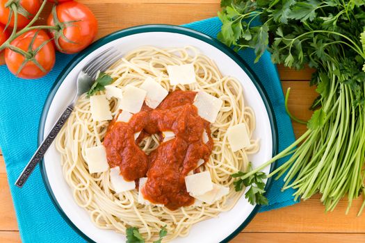 Delicious plate of spaghetti pasta garnished with grana padano cheese, italian parsley and red sauce surrounded by tomatoes and fork on napkin