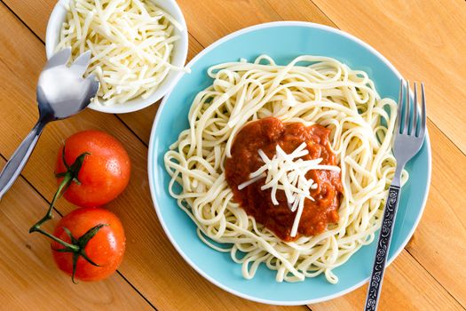 Top down first person perspective view on blue bowl of pasta topped with red sauce next to gruyere cheese in dish and cherry tomatoes