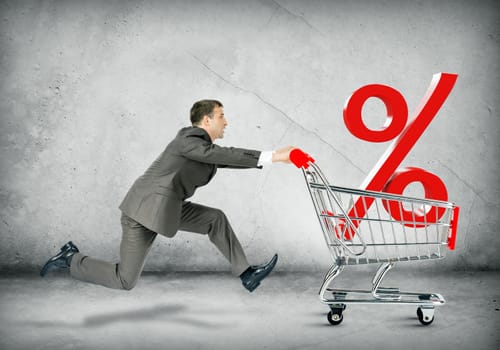 Businessman pushing shopping cart with percentage sign on grey background