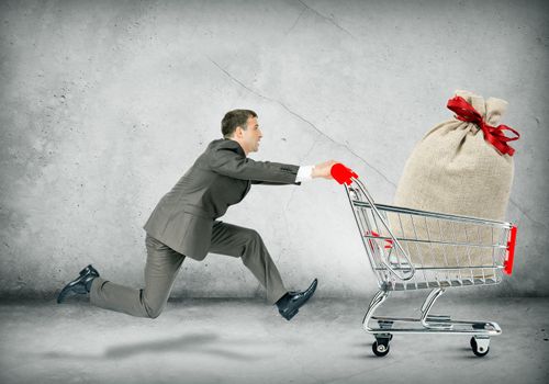 Businessman pushing shopping cart with money bag on grey background