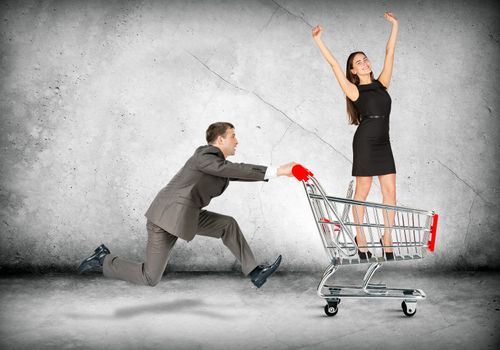 Businessman pushing shopping cart with business lady on grey background