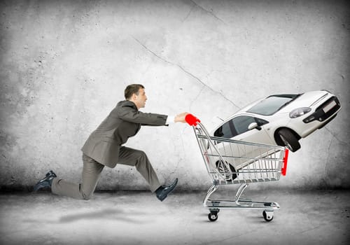 Businessman pushing shopping cart with car on grey background