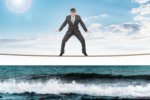 Businessman on rope looking down on sea waves, danger concept