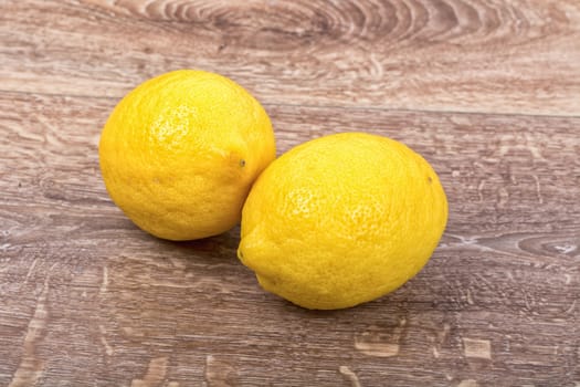 Two yellow lemons on the brown wooden background