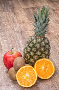 Orange oranges, pineapple, kiwi and apple on a brown wooden background