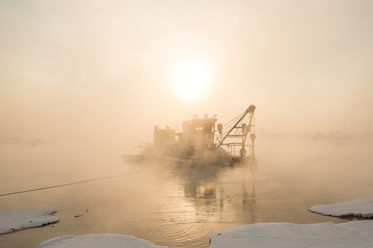 a dredger boat in winter mist at sunset