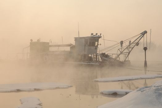 a dredger boat in winter mist at sunset