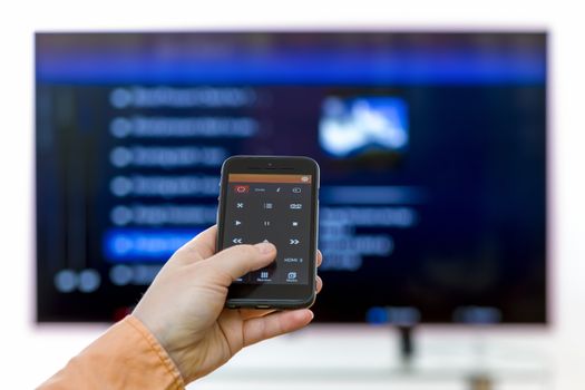 Closeup on woman hand holding smartphone and use a app with remote control  and surfing programs on television. Focus on the remote control.