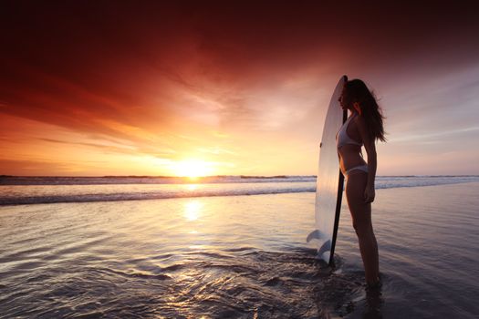 Beautiful surfer woman on the beach at sunset