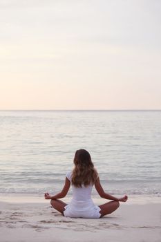 Woman in lotus yoga pose at sunrise on the beach