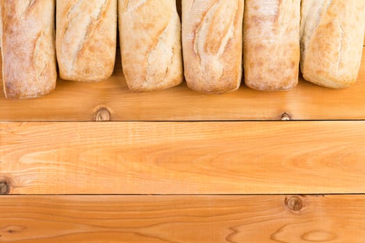 Crusty fresh bread loaf border arranged in a line on a wood background with copyspace showing the ends of the loaves viewed from above
