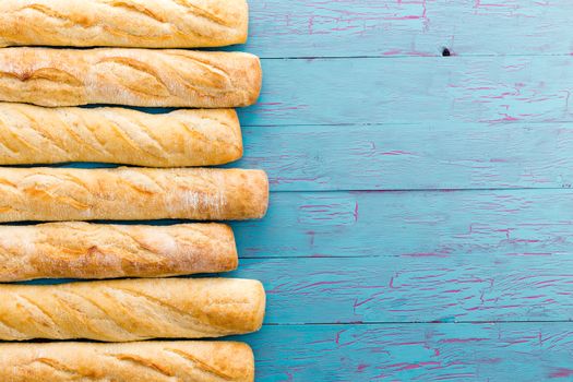 Border formed of a row of crusty freshly baked French baguettes arranged on the side over a rustic blue wood background with copy space, view from above
