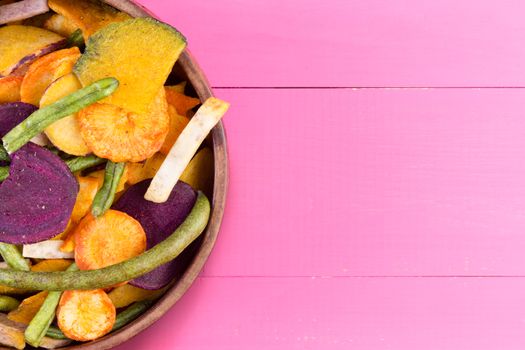 Bowl of dried fresh vegetable chips for a healthy organic finger snack full of vitamins and dietary fiber on an exotic vibrant pink tropical background with copy space