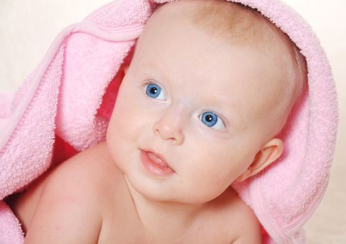 Adorable baby girl looking  under a pink towel