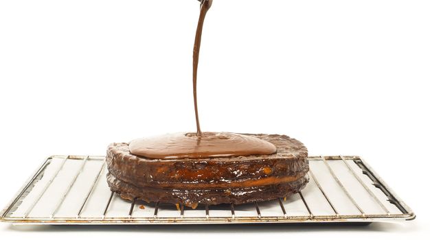 Closeup of chocolate icing pouring over Sacher torte towards white