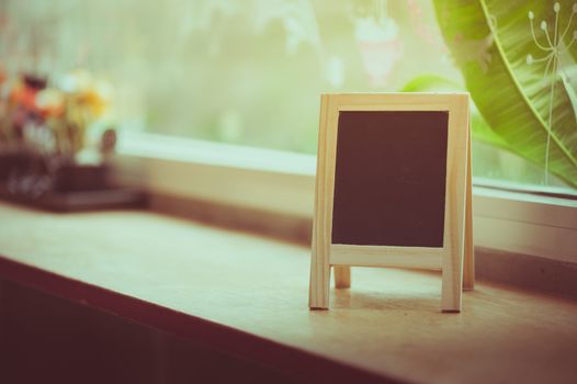 Small A-frame black board with blank area for text or message on wood bar in cafe wih vintage filter effect