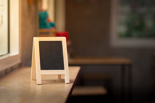 Small A-frame black board with blank area for text or message on wood bar in cafe at morning time