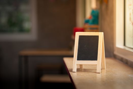 Small A-frame black board with blank area for text or message on wood bar in cafe at morning time