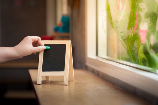 Woman left hand writing on small A-frame black board with blank area for text or message on wood bar in cafe