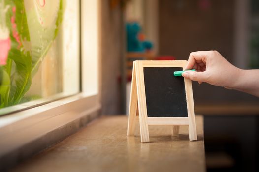 Woman right hand writing on small A-frame black board with blank area for text or message on wood bar in cafe