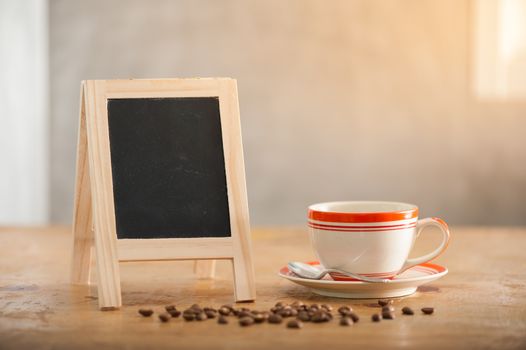 Small A-frame black board with blank area for text or message and coffee cup on wood table in morning time