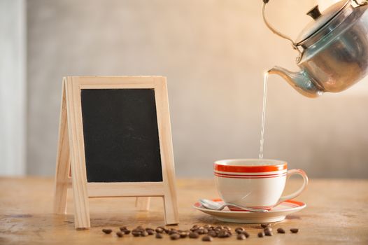 Small A-frame black board with blank area for text or message with coffee cup on wood table