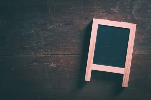 Small A-frame black board with blank area for text or message on rustic wood table with low key scene and vintage filter effect