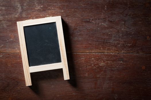 Small A-frame black board with blank area for text or message on rustic wood table with low key scene.