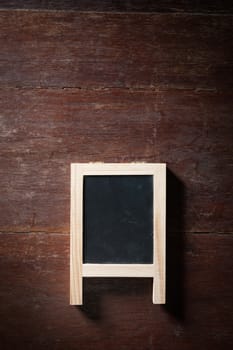 Small A-frame black board with blank area for text or message on rustic wood table with low key scene.