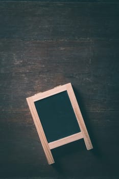 Small A-frame black board with blank area for text or message on rustic wood table with low key scene and vintage filter effect