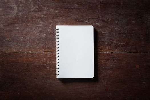 Small opened notepad with blank area for text or message and pen on rustic wood table with low key scene and vinatage filter effect