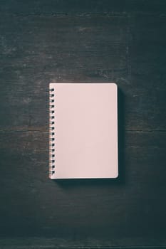 Small opened notepad with blank area for text or message and pen on rustic wood table with low key scene and vinatage filter effect