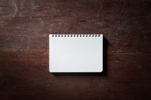 Small opened notepad with blank area for text or message and pen on rustic wood table with low key scene.