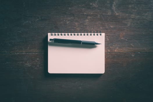 Small opened notepad with blank area for text or message and pen on rustic wood table with low key scene and vinatage filter effect