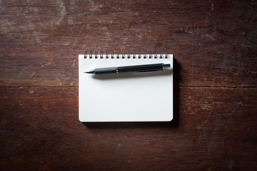 Small opened notepad with blank area for text or message and pen on rustic wood table with low key scene.