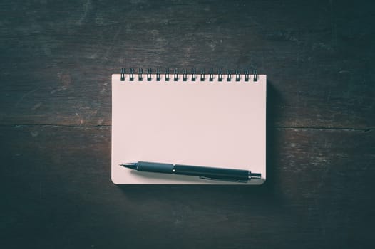 Small opened notepad with blank area for text or message and pen on rustic wood table with low key scene and vinatage filter effect