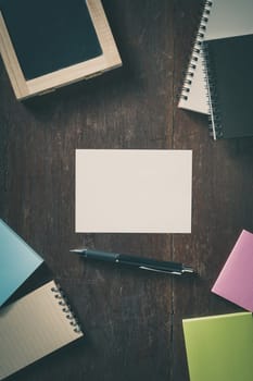 Blank paper with area for text or message, pen, notebook, and sticky paper on wood table with low key scene and vintage filter effect