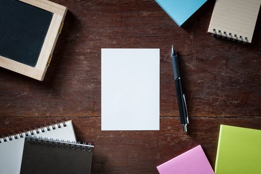 Blank paper with area for text or message, pen, notebook, and sticky paper on wood table with low key scene