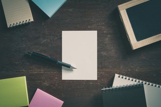 Blank paper with area for text or message, pen, notebook, and sticky paper on wood table with low key scene and vintage filter effect