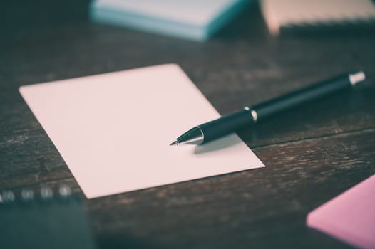 Blank paper, pen, notebook, and sticky paper on wood table with vintage filter effect