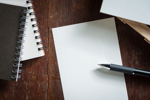 Blank paper on wood table with notebooks on wood table with low key scene