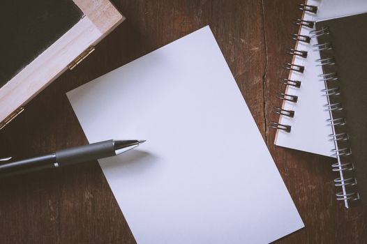 Blank paper on wood table with notebooks on wood table with vintage filter effect
